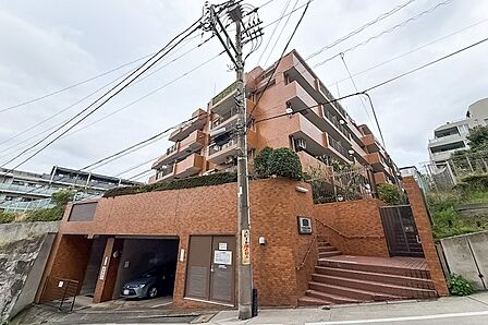 新耐震基準に適合した、1985年竣工、地上5階建てのマンション。傾斜地に建っているため、エントランスの前には階段があります。レンガ色のタイル貼りが目を惹く、どっしりとした外観です。