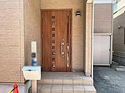木目調の玄関ドアとレンガ調の外壁が温かみのあるエントランスです。ドアのガラス部分から自然光を取り込み、明るい空間を保ちます。機能的な門柱を備え、奥には外回りの収納に役立つ物置も設置されています。