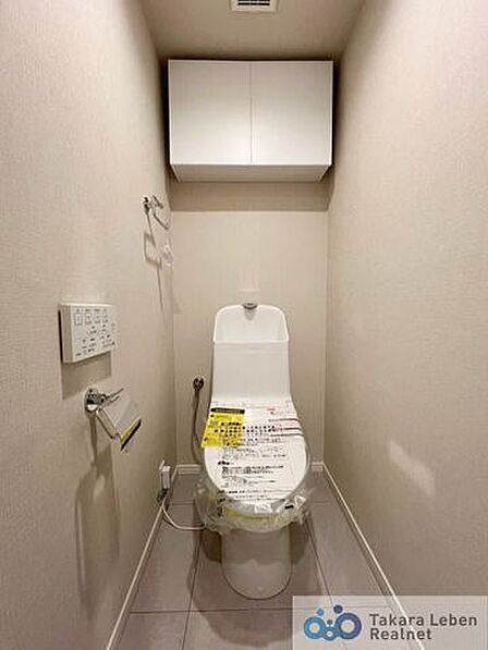 温水洗浄便座付きトイレ。ペーパーホルダーやタオル掛けは標準装備しています。また、上部には吊戸棚があるので、トイレットペーパーのストックや清掃道具等を収納するのに便利です。