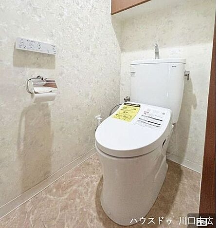 温水洗浄便座を備えた清潔感のあるトイレ空間です。上部には備品を収納できるキャビネットを設け、日常の利便性と整頓のしやすさに配慮した造りです。