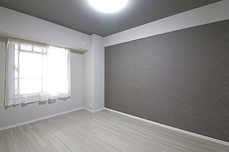 グレーのアクセントクロスと、同系色でまとめられた天井が空間を引き締めるモダンな意匠。明るい木目調のフローリングがスマートに調和し、スタイリッシュなデザインが際立つシンプルな洋室です。