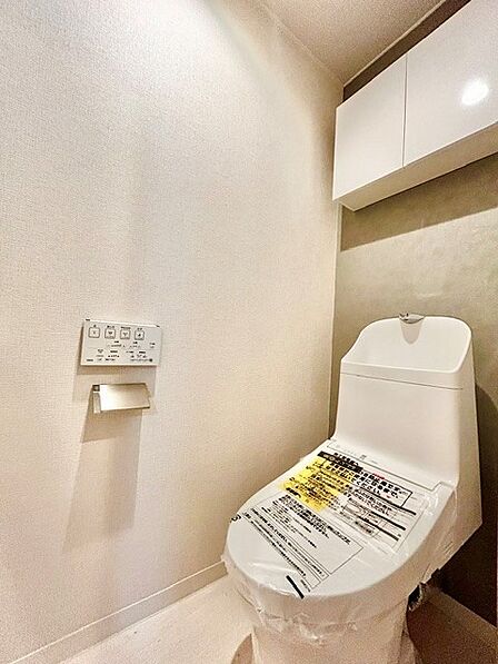 手洗い一体型で清潔感のある温水洗浄便座付きトイレ!上部にはトイレットペーパーや掃除用品を隠して収納できる便利な吊戸棚を設置。シックなアクセントクロスがおしゃれで落ち着く快適な個室空間です。