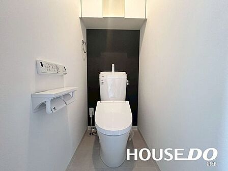 温水洗浄便座付きのトイレ。収納スペースを備え、トイレットペーパーや掃除用品をすっきり整理できます。背面のアクセントクロスが空間のデザイン性を高め、落ち着いた印象を演出します。