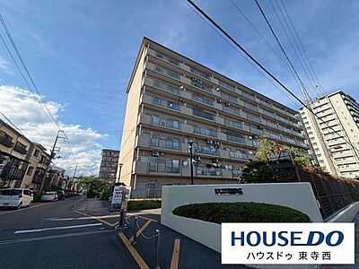 外観：大型の分譲マンション。敷地前の道路は見通しがよく、建物前に植栽帯が整えられています。周囲は落ち着いた住宅街で、生活しやすい環境です。