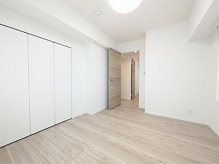 白を基調とした内装に木目調のドアが映える、スタイリッシュな洋室。壁一面に大容量のクローゼットを備えており、衣類や小物をすっきり収納できます。廊下へと繋がる開放的で生活動線の良い間取りです。