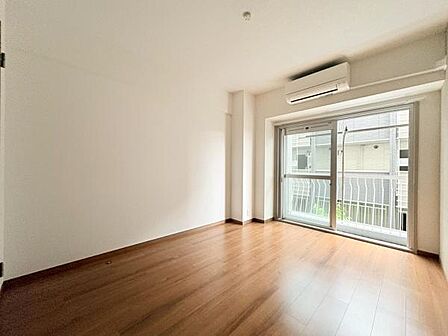 大きな窓から自然光が入り室内が明るくなっています。フローリングの床が清潔感を感じさせます。壁や天井もシンプルで使いやすい印象です。エアコンが設置されているので快適な室温調整が可能です。