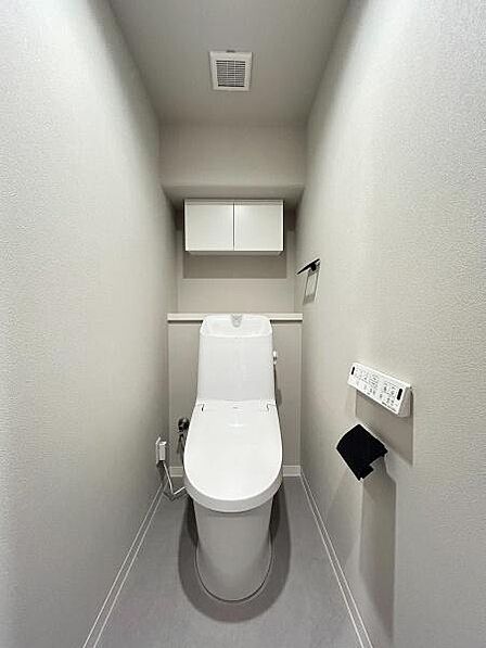 背面の高い位置には扉付きの吊り戸棚が設置されており、トイレットペーパーや掃除用具などをすっきりと目隠し収納できます。壁面のリモコン操作やペーパーホルダーなども使いやすい配置です。