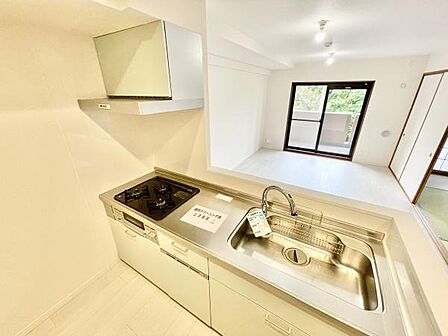 白を基調とした明るいキッチンです。広々としたシンクと作業スペースが確保されています。使いやすい三口コンロが設置されています。対面式で開放感を感じられます。シンプルなデザインで日々の家事が快適です。