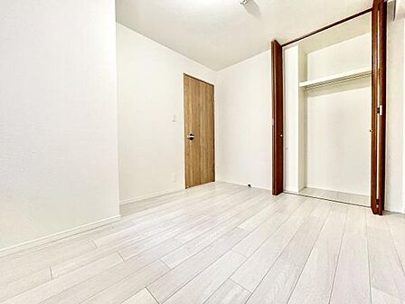 明るい色合いのフローリングが広がる洋室です。クローゼット付きで収納スペースも確保されています。ドアやクローゼットの木目デザインがアクセントになっています。