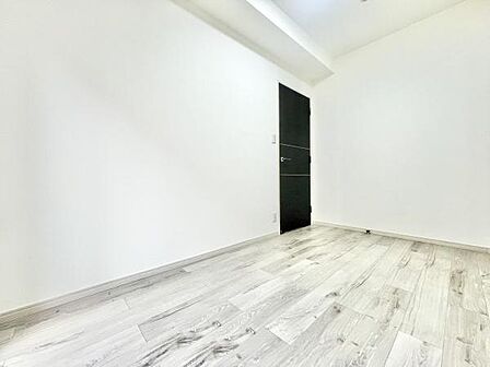 明るい色合いのフローリングが特徴の洋室です。シンプルで無駄のない空間が印象的です。壁や床のデザインが室内をすっきりと見せます。黒いドアがアクセントとなっています。