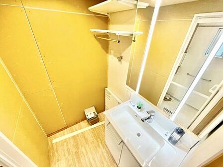 明るい照明が特徴的な洗面台・洗面所です。清潔感のある白を基調としたデザインが印象的です。収納棚も設置されており整理整頓に便利です。床材と壁材のコントラストがおしゃれな印象を与えます。
