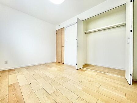 明るいフローリングが印象的な寝室です。クローゼットが広く収納スペースがしっかりと確保されています。ドアや収納扉はナチュラルな木目調で揃えられています。全体的に清潔感のある室内です。