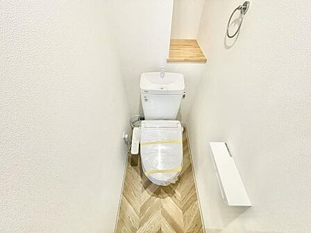 トイレはシンプルで清潔感のある内装です。壁面のホルダーやタオルリングが備え付けられ使い勝手の良い空間となっています。奥には小物を置ける棚が設けられており便利に利用できます。