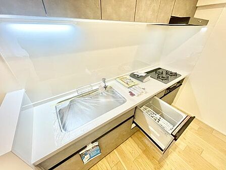 明るく清潔感のあるキッチンです。作業スペースが広くお手入れもしやすい仕様です。食器洗浄機やガスコンロも設置されており効率的に調理できます。木目調の床が温かみを演出しています。