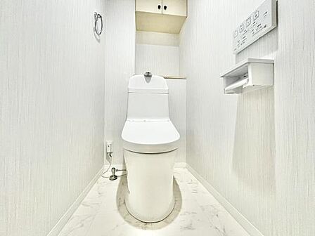 白を基調とした清潔感のあるトイレです。壁面収納が設置されすっきりとした空間を実現しています。ペーパーホルダーやリモコンが壁に設置され使い勝手にも配慮されています。