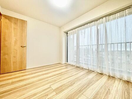 大きな窓から明るい光が差し込む寝室です。シンプルな内装でどんな家具も合わせやすい雰囲気です。バルコニーに面しているため開放感もあります。木目調の床が温かみを感じさせます。清潔感のある空間です。