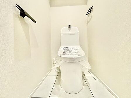 白を基調とした清潔感のあるトイレです。シンプルな内装が落ち着いた雰囲気を演出しています。壁付けのペーパーホルダーが両側に配置されています。ゆとりのある空間設計が特徴です。