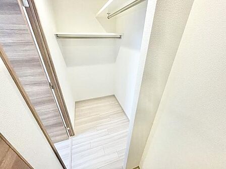 扉を開けてすぐに使いやすい収納スペースです。シンプルな内装で清潔感があります。ハンガーパイプと棚が備え付けられ収納しやすい設計となっています。床は明るい色合いで室内に統一感を与えます。