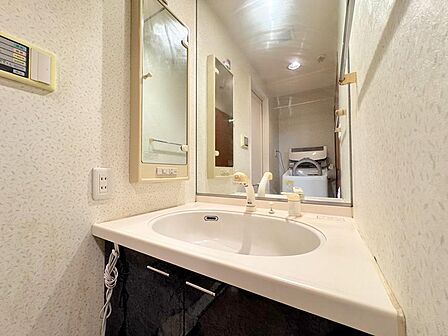 身支度に便利な大型鏡を備えた洗面化粧台。洗面ボウルが広く、日々のお手入れや部分洗いも快適です。収納付きの鏡や足元のキャビネットで小物もすっきり。奥には洗濯機置き場があり、家事動線にも配慮されています。