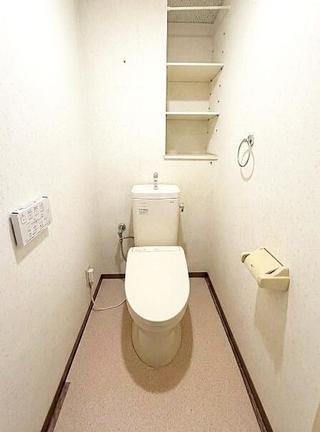 【一部AIによるモノ消し済み】壁面に収納棚が設けられており整理整頓がしやすいトイレです。温水洗浄便座が付いている点も特徴的です。