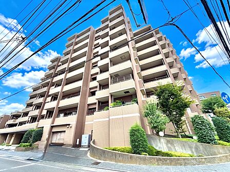 多層階のマンション外観、青空の下で敷地内に植栽あり