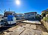 外観：建物前の舗装された敷地と周囲の住宅