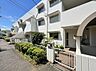 外観：植栽のある白い外壁の集合住宅と前面道路