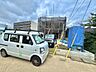 外観：建物前の道路と青いフェンス、駐車車両