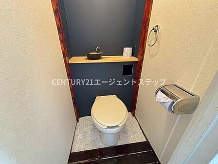 落ち着いた色合いの壁面が特徴的なトイレです。コンパクトにまとめられているため空間を有効に使うことができます。棚が設けられており小物の配置にも便利です。手洗い器も設置されています。