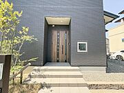 重厚感のある玄関扉が建物全体の雰囲気に調和しています。ステップやアプローチ部分も広々としており開放感を感じられます。外壁のシックなカラーと木目の扉がモダンな印象を与えます。