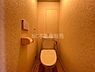 トイレ：温かみのある照明が特徴のトイレです。壁面の質感が落ち着いた印象を与えます。ペーパーホルダーと操作パネルがすっきりと配置されています。シンプルな空間設計です。清掃も行き届いています。