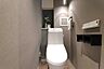 トイレ：落ち着いた色合いの壁紙と洗練されたデザインのトイレが印象的です。使い勝手の良い収納棚や手洗いスペースも確保されています。照明がやわらかく空間に統一感があります。設備が整っておりシンプルな雰囲気です。